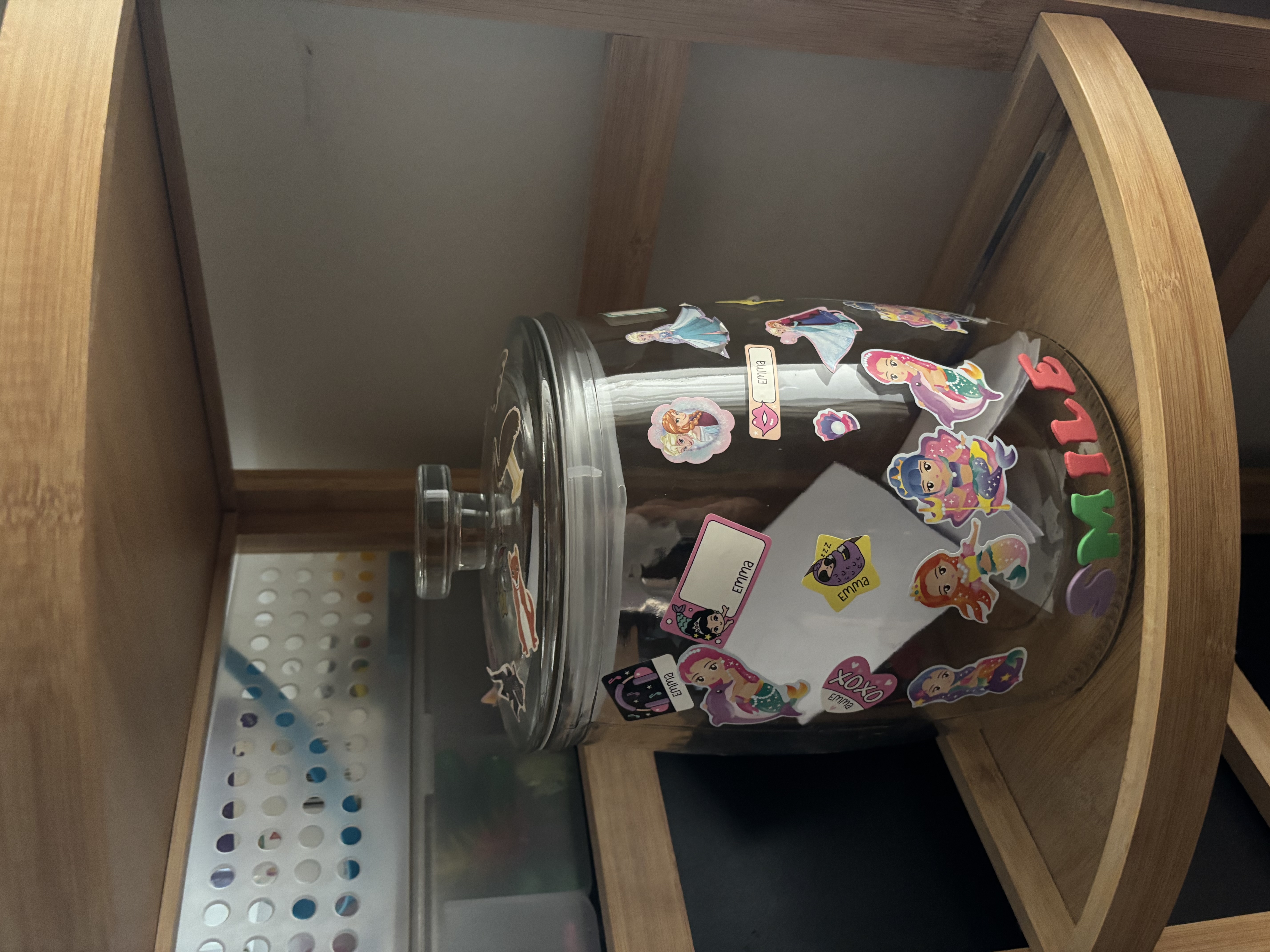 A jar on a shelf with stickers on it.